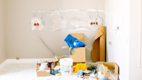 A room undergoing renovation with tools, supplies, wiring, and paint cans scattered around