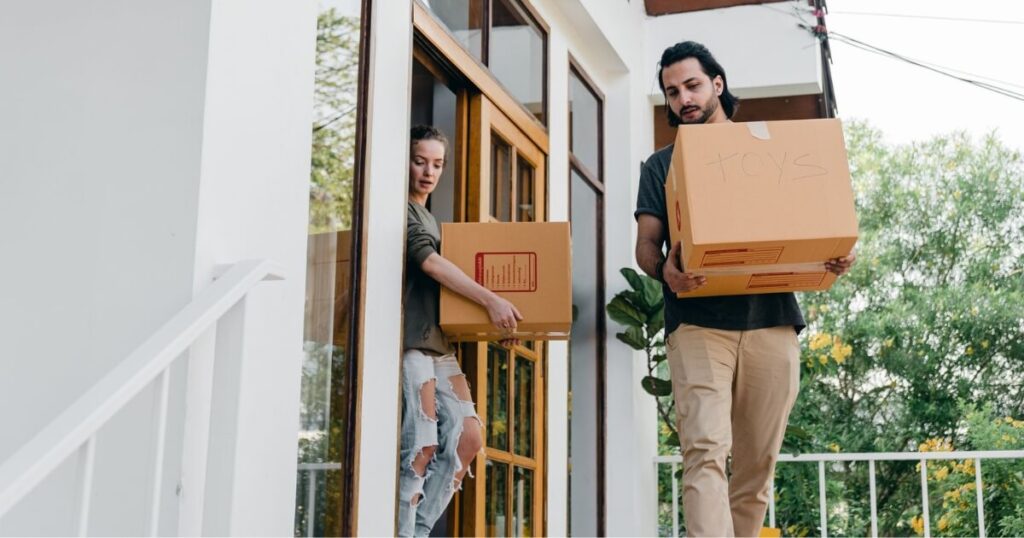 A young couple carrying boxes out of their modern home on moving day