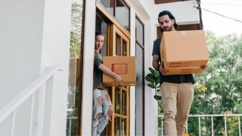 A young couple carrying boxes out of their modern home on moving day