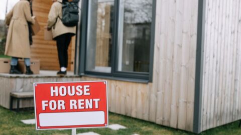 A couple entering a modern wooden house for rent, carrying boxes