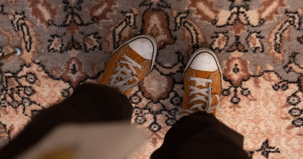 Top-down view of orange sneakers standing on an ornate vintage-patterned carpet indoors