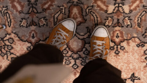 Top-down view of orange sneakers standing on an ornate vintage-patterned carpet indoors