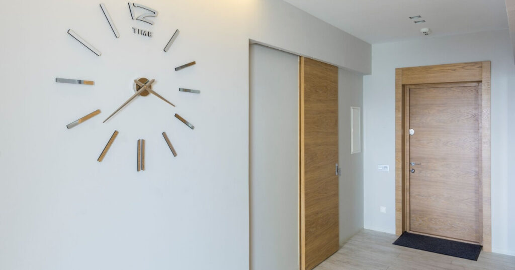 An aprtment hallway with two apartment doors and a clock visible on the wall