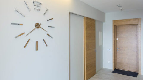 An aprtment hallway with two apartment doors and a clock visible on the wall