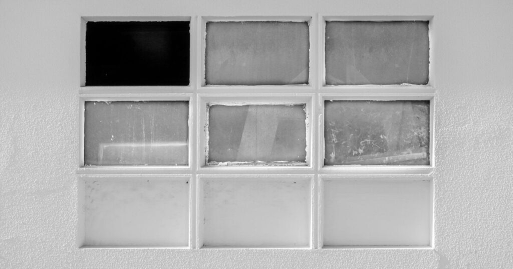 9 windows on a white wall with one broken