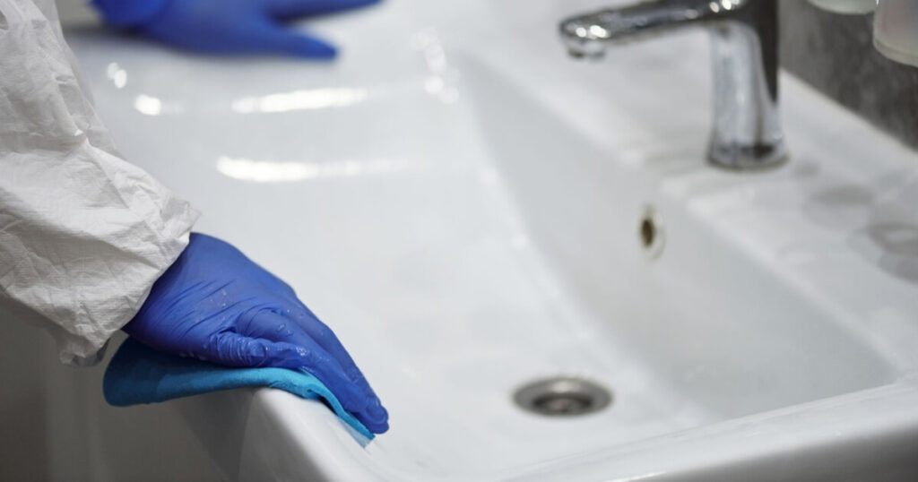 Hands wearing blue gloves cleaning a bathroom sink