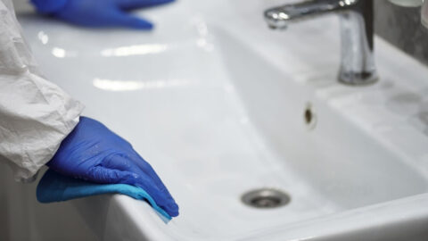 Hands wearing blue gloves cleaning a bathroom sink