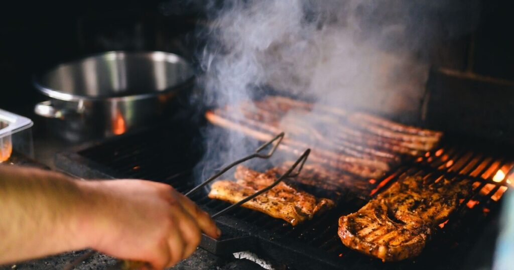 Close-up of grilling meat with smoke rising on a barbecue