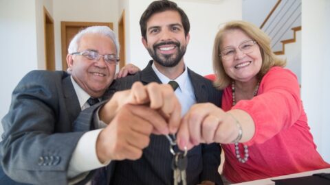 Smiling elderly couple receiving house keys from realtor indoors