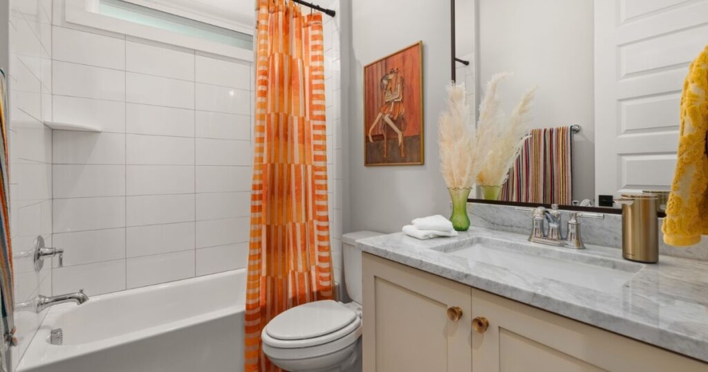 Bright bathroom featuring an orange-striped shower curtain and a marble countertop for a modern look