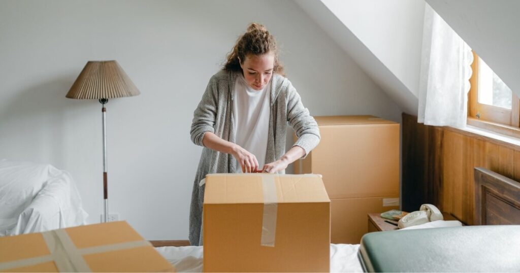 A young woman unpacking cardboard boxes in a peaceful attic room with natural daylight