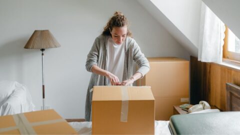 A young woman unpacking cardboard boxes in a peaceful attic room with natural daylight