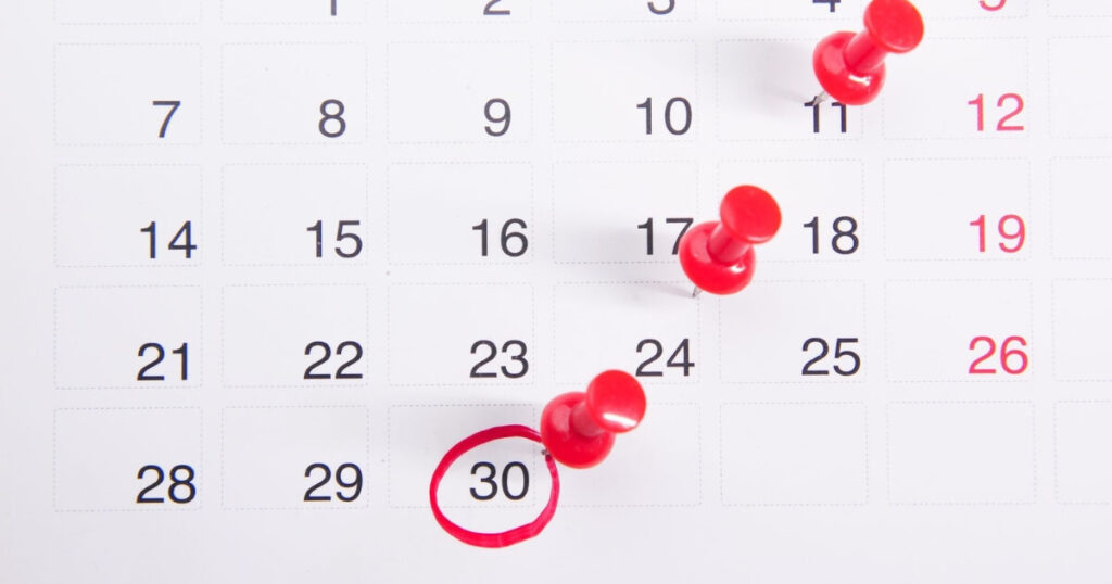 Close-up of a calendar with red push pins marking important dates, with the 30th date circled in red