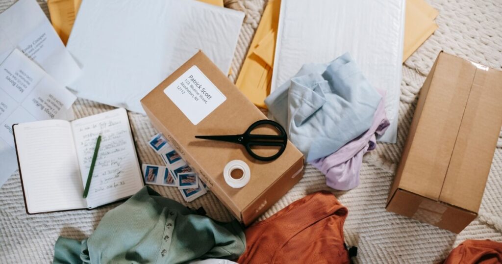 A neatly arranged set of packing materials including boxes, envelopes, and clothing on a carpet