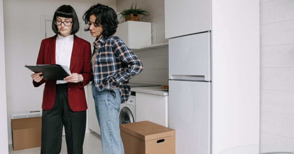 Two women reviewing documents in a kitchen amid moving boxes