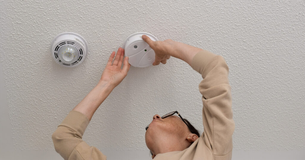 A man inspecting the smoke alarm on the ceiling