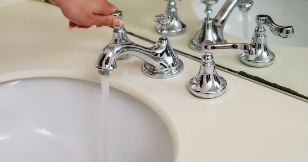 Hand operating a chrome faucet with running water in an elegant bathroom setting