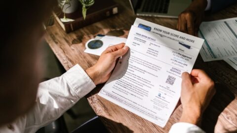 An adult man examining a financial document under natural light at a wooden desk