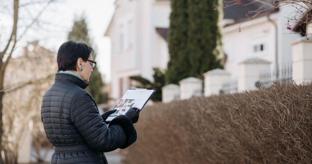 Landlord assessing house with clipboard during winter season outdoors