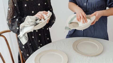 Women drying ceramic bowls and setting a table with plates and napkins