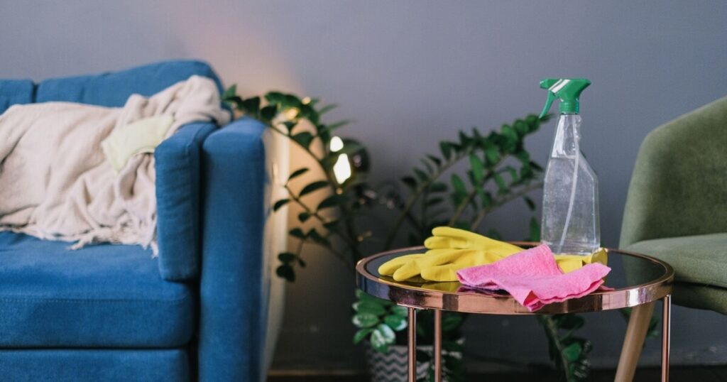 Modern living room with cleaning supplies on a table, featuring a blue sofa and indoor plants
