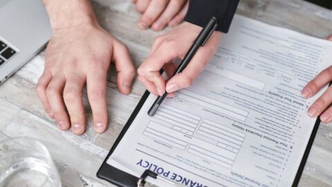 Close-up image of two people signing an insurance policy document on a wooden desk