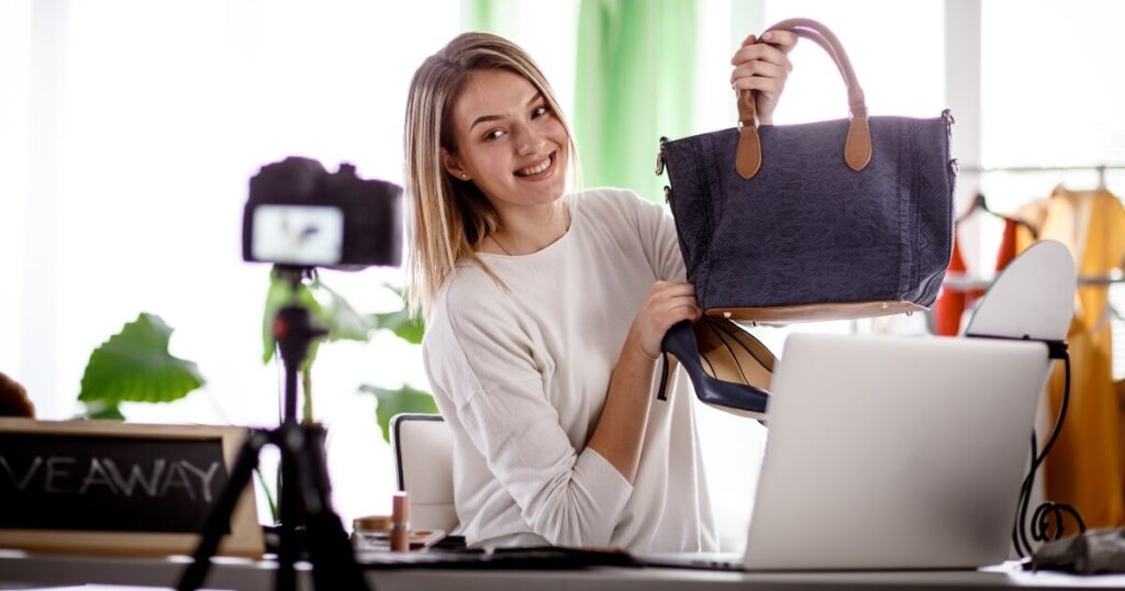 Woman filming herself holding a handbag, next to her laptop