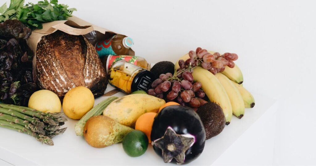 A colourful assortment of fresh fruits and vegetables including bread and organic produce on a white background