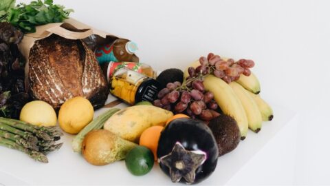 A colourful assortment of fresh fruits and vegetables including bread and organic produce on a white background