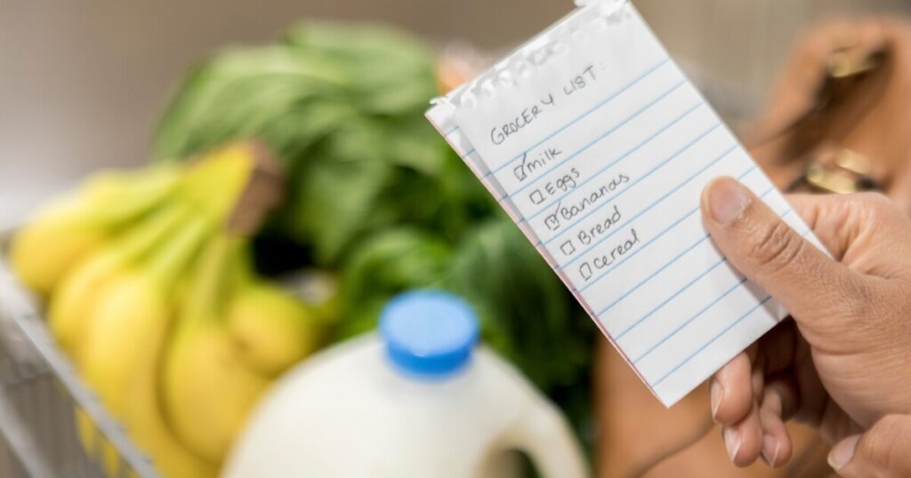 A hand holding a paper grocery list