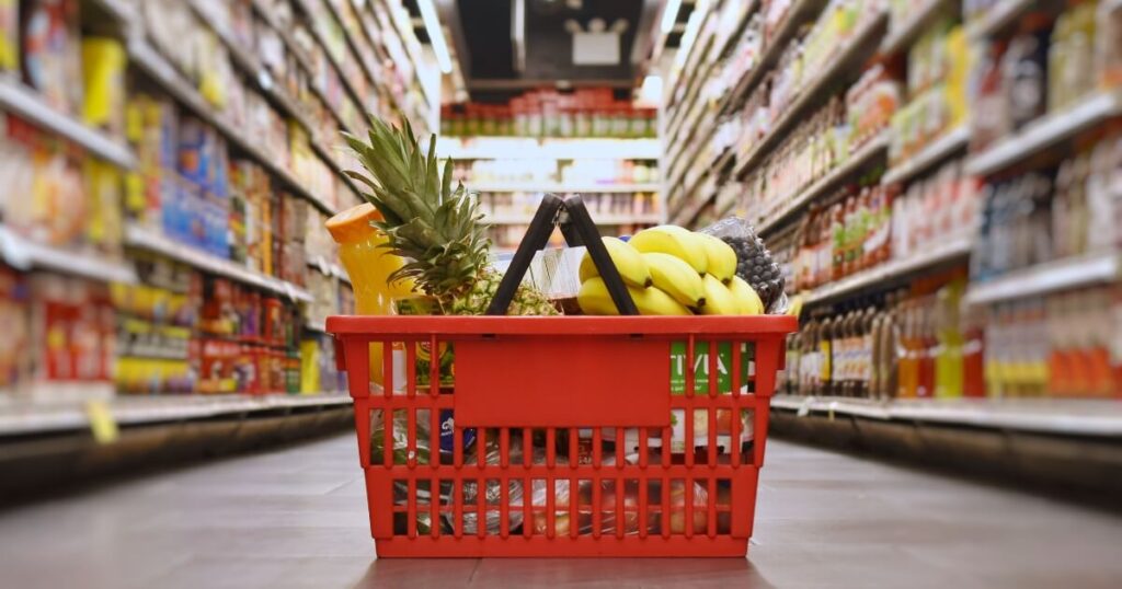 A red shopping basket full of groceries for the week on the floor between two aisles at the supermarket