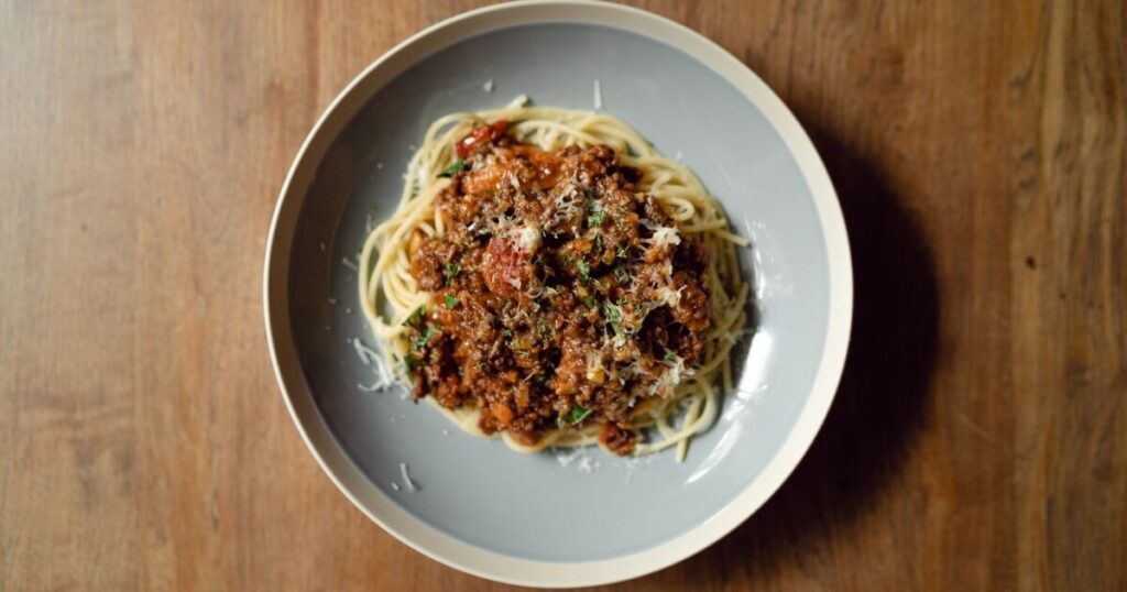 Top view of appetizing spaghetti bolognese with parmesan cheese on a wooden table