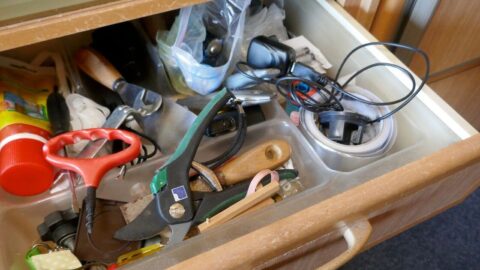 Cluttered apartment junk drawer filled with everyday essentials including pruning shears, tape, cords, and small hand tools.