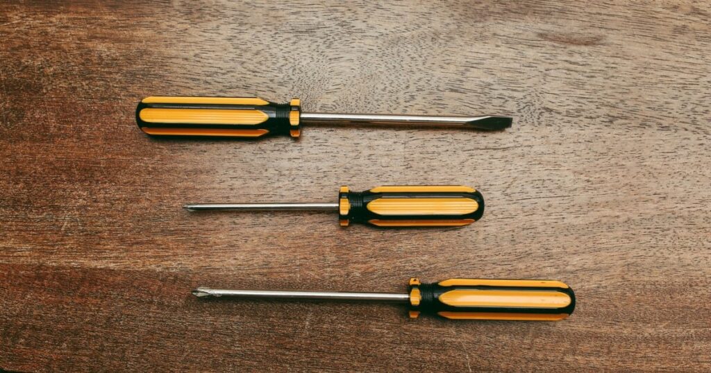 Three yellow and black screwdrivers with flathead and Phillips tips laid out on a dark wooden surface.