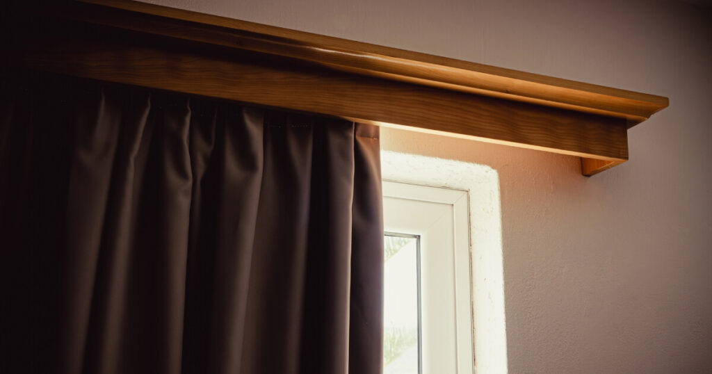 Grey blackout curtains hanging from a wooden curtain rod, with a section of window showing behind