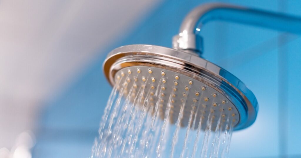 A metal shower head in a blue bathroom with water running out of the head