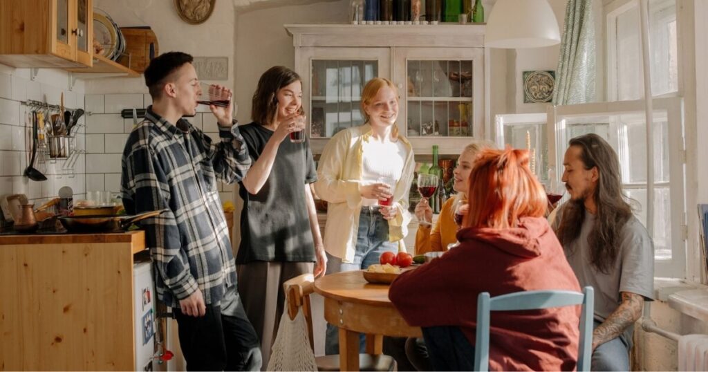 A group of friends laughing and enjoying drinks in a kitchen setting