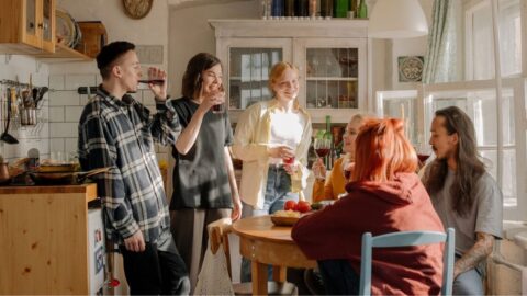A group of friends laughing and enjoying drinks in a kitchen setting