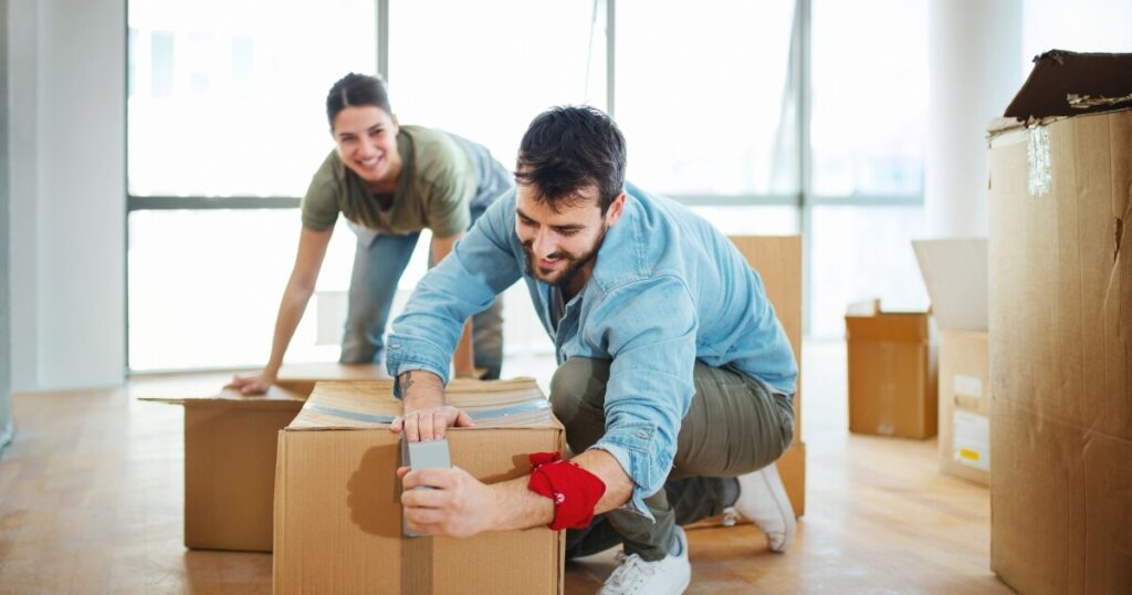 A man and woman taping up cardboard boxes during moving day