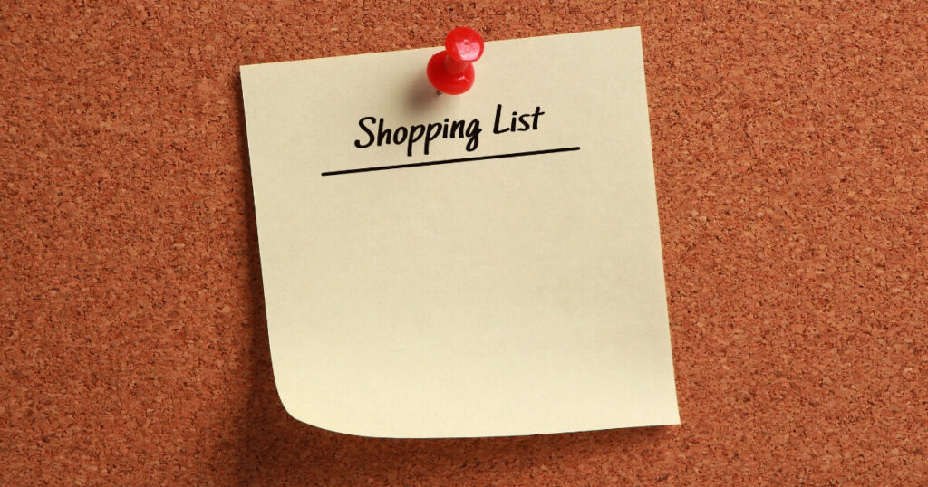 A yellow post-in note on a cork board with the title Shopping List underlined